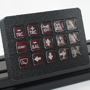 Könnte beinhalten: Schwarzes Tastenfeld mit durchsichtigen Tasten, die mit verschiedenen Funktionen beschriftet sind, darunter "TRC", "IGN", "ABS", "BAL", "SORRY" und "ESC".