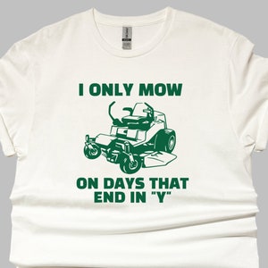 May include: White t-shirt with green text and a graphic of a riding lawnmower. The text reads "I only mow on days that end in "Y""
