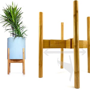 May include: A natural bamboo plant stand with four legs and a square top. The stand is made of natural bamboo and has a light brown color. The stand is adjustable in width and can be used to display plants of different sizes. The stand is made by Sariwa.