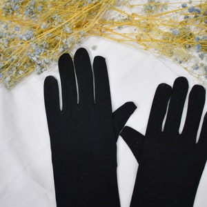 May include: A pair of solid black, elbow-length gloves featuring a smooth, opaque fabric construction. The gloves are designed with individual finger sections and extend past the wrist, providing full hand and forearm coverage with a clean, seamless look.