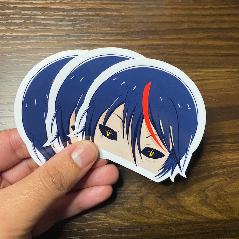 K&ouml;nnte beinhalten: Drei wei&szlig;e Aufkleber mit einem schwarzen und blauen Anime-Charakter mit gelben Augen. Der Charakter hat einen roten Streifen im Haar.