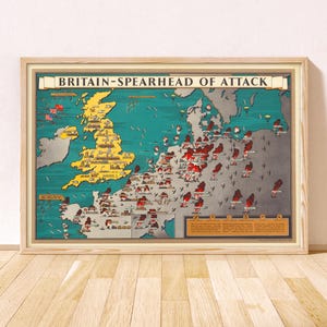 May include: A framed historical map titled BRITAIN-SPEARHEAD OF ATTACK, featuring a yellow Great Britain and a grey continental Europe. The map displays red explosion icons, military symbols, and aircraft illustrations across the sea and land.