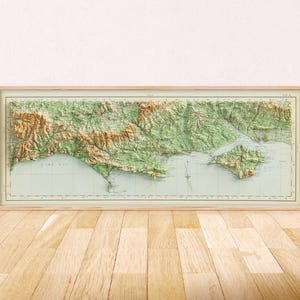 May include: A rectangular framed relief map featuring a topographical representation of a coastal region with green landmasses, brown mountain ranges, and light blue water, all enclosed within a light-colored wooden frame.