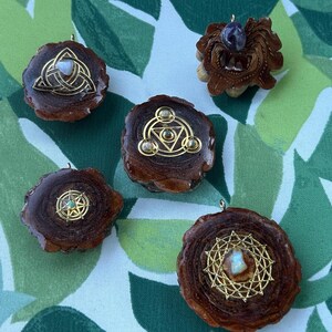 May include: A selection of handcrafted wooden pendants with gold-coloured metal accents. Each pendant features a unique design, including geometric shapes and a central stone. The pendants are displayed on a green and white patterned background.