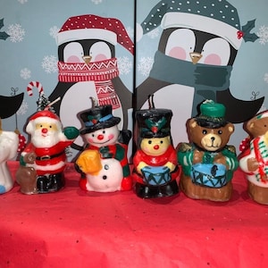 Può includere: Set di sette figurine di candele natalizie, tra cui un pupazzo di neve, Babbo Natale, un angelo, un tamburino, un orso e due orsi con cappelli di Babbo Natale. Le figurine sono in cera e hanno un aspetto vintage.