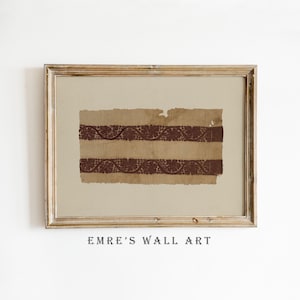 May include: Framed wall art featuring a vintage textile fragment. The artwork displays two horizontal bands of dark brown floral patterns on a tan background. The frame is a light brown color, and the text "EMRE'S WALL ART" is printed at the bottom.