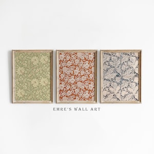 Peut inclure: Trois impressions encadrées avec différents motifs floraux. Les impressions sont dans un cadre en bois clair et ont un fond blanc. La première impression a un fond vert avec des fleurs blanches. La deuxième impression a un fond orange avec des fleurs blanches. La troisième impression a un fond bleu avec des fleurs blanches. Le texte "EMRE'S WALL ART" est sous les impressions.