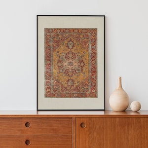 May include: A framed print of a vintage rug with a red, yellow and blue geometric pattern. The print is hanging on a white wall above a wooden dresser.