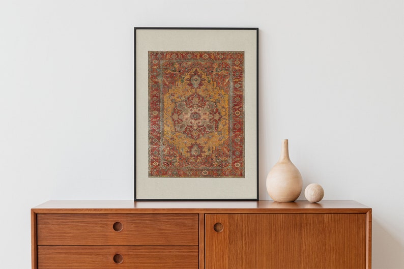 May include: A framed print of a vintage rug with a red, yellow and blue geometric pattern. The print is hanging on a white wall above a wooden dresser.