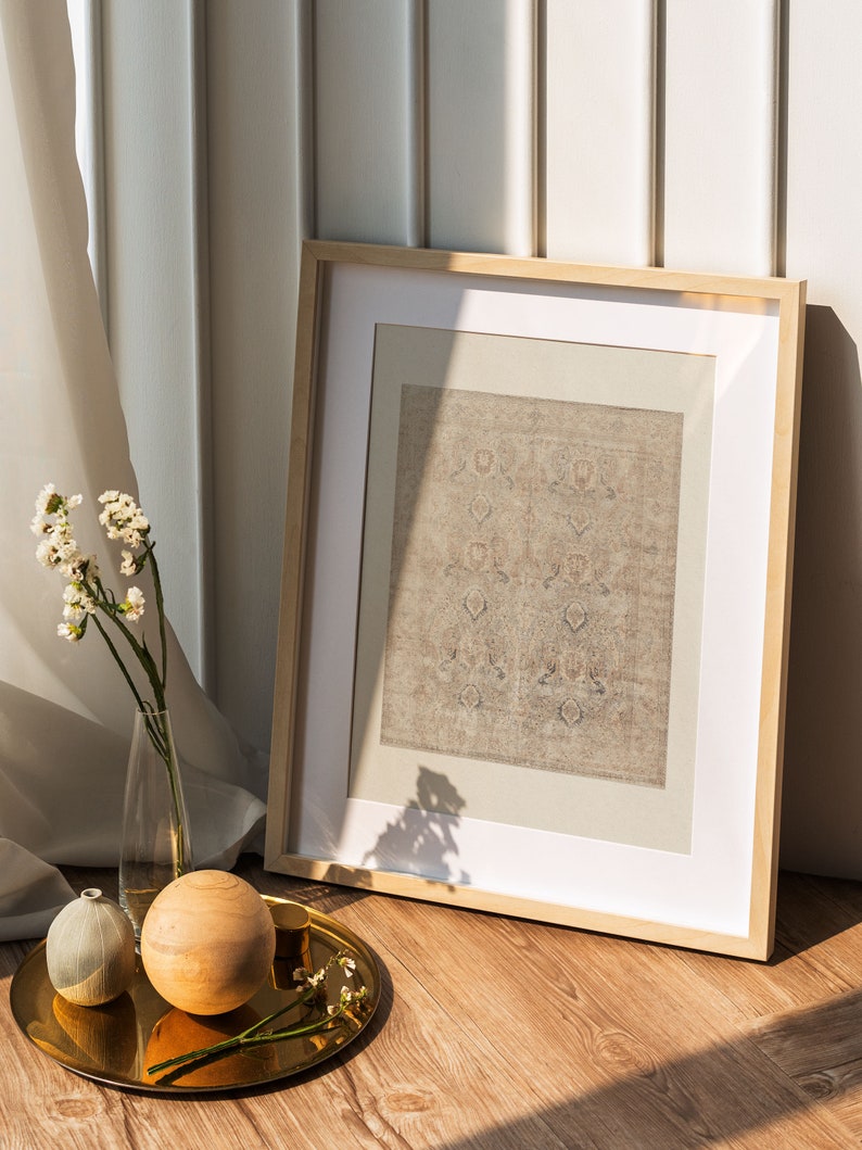Puede incluir: Un cuadro con marco de madera con un estampado beige con motivos en su interior. El marco est&aacute; sobre un suelo de madera junto a una bandeja dorada con una esfera de madera, un jarr&oacute;n peque&ntilde;o y unas ramitas de flores blancas.