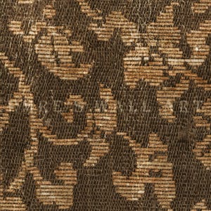 May include: Close-up of a woven fabric with a repeating pattern in shades of brown and tan. The design features stylized floral or geometric shapes, creating a textured surface. The fabric appears to be vintage or antique.