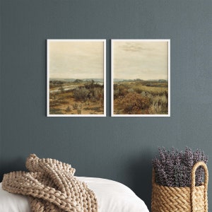 May include: Two framed landscape paintings with a muted color palette. The paintings depict a grassy field with a river running through it. The sky is a light blue with some clouds.