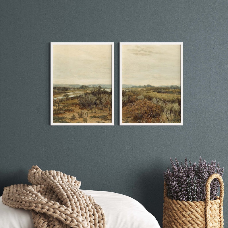 May include: Two framed landscape paintings with a muted color palette. The paintings depict a grassy field with a river running through it. The sky is a light blue with some clouds.