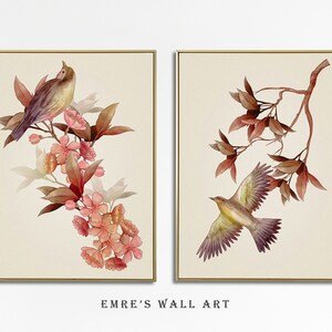 May include: Two framed watercolor paintings with a bird and floral motif. The first painting features a brown and yellow bird perched on a branch with pink flowers. The second painting features a brown and yellow bird in flight with brown leaves.