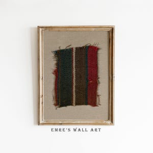 May include: A framed piece of woven fabric with red, green, and brown stripes. The fabric is frayed at the edges and has a rustic, vintage look. The frame is a simple, light wood.