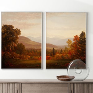 May include: A pair of framed landscape paintings depicting a scenic view of a valley with rolling hills, trees, and a distant mountain range. The paintings are in a muted color palette of browns, greens, and blues, with hints of red and orange in the foliage.