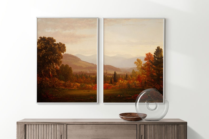 May include: A pair of framed landscape paintings depicting a scenic view of a valley with rolling hills, trees, and a distant mountain range. The paintings are in a muted color palette of browns, greens, and blues, with hints of red and orange in the foliage.