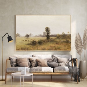 May include: A framed landscape painting depicting a rural scene with a grassy field, trees, and a cloudy sky. The painting is in a light wood frame and is hanging on a wall.
