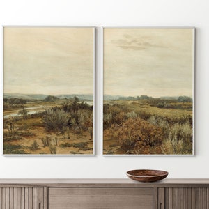 May include: A pair of framed landscape paintings depicting a river flowing through a field of tall grass and trees under a cloudy sky.