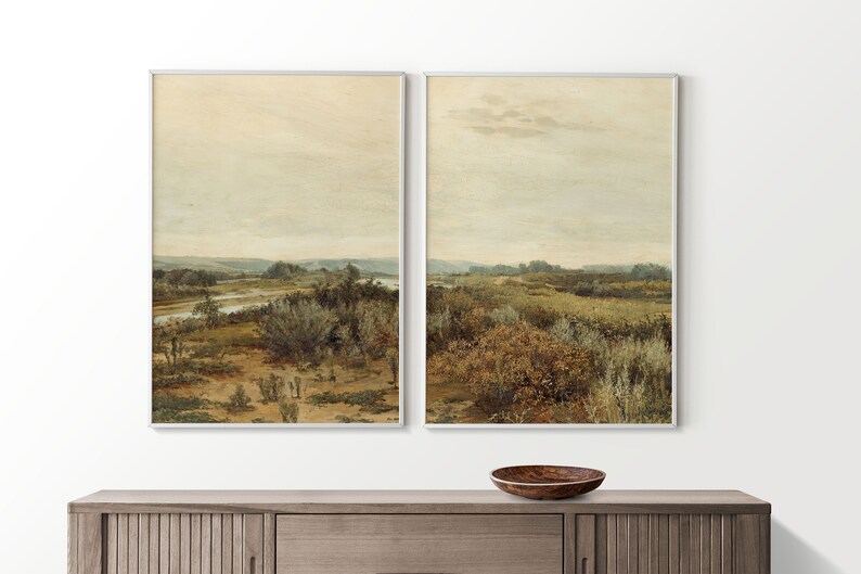 May include: A pair of framed landscape paintings depicting a river flowing through a field of tall grass and trees under a cloudy sky.