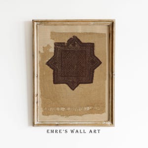 May include: Framed wall art featuring a brown star-shaped design on a tan background. The artwork has a distressed, vintage aesthetic, with visible fabric texture and a wooden frame. The text "EMRE'S WALL ART" is printed at the bottom.