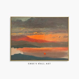 Puede incluir: Un cuadro de paisaje rectangular en un marco dorado fino que representa una puesta de sol sobre una masa de agua con nubes oscuras, cielo naranja y rojo y colinas lejanas. Un pequeño círculo rojo brillante está sobre el agua. Texto EMRE'S WALL ART.