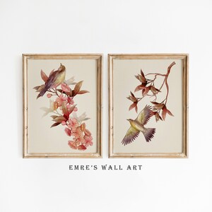 May include: Two framed watercolor prints with a floral and bird theme. The print on the left features a small bird perched on a branch of pink flowers. The print on the right features a bird in flight with a branch of brown leaves.