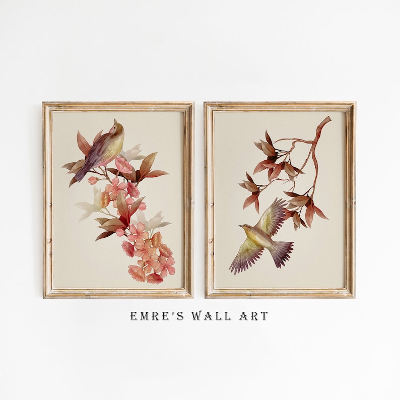 May include: Two framed watercolor prints with a floral and bird theme. The print on the left features a small bird perched on a branch of pink flowers. The print on the right features a bird in flight with a branch of brown leaves.