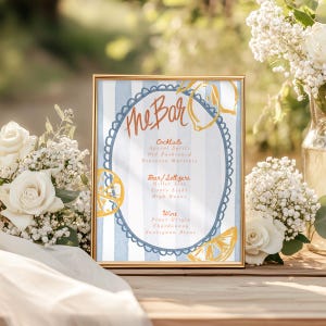 May include: A gold-framed sign with a blue and white striped background and a lemon illustration. The sign reads "The Bar" and lists cocktails, beer, seltzers, and wine options.