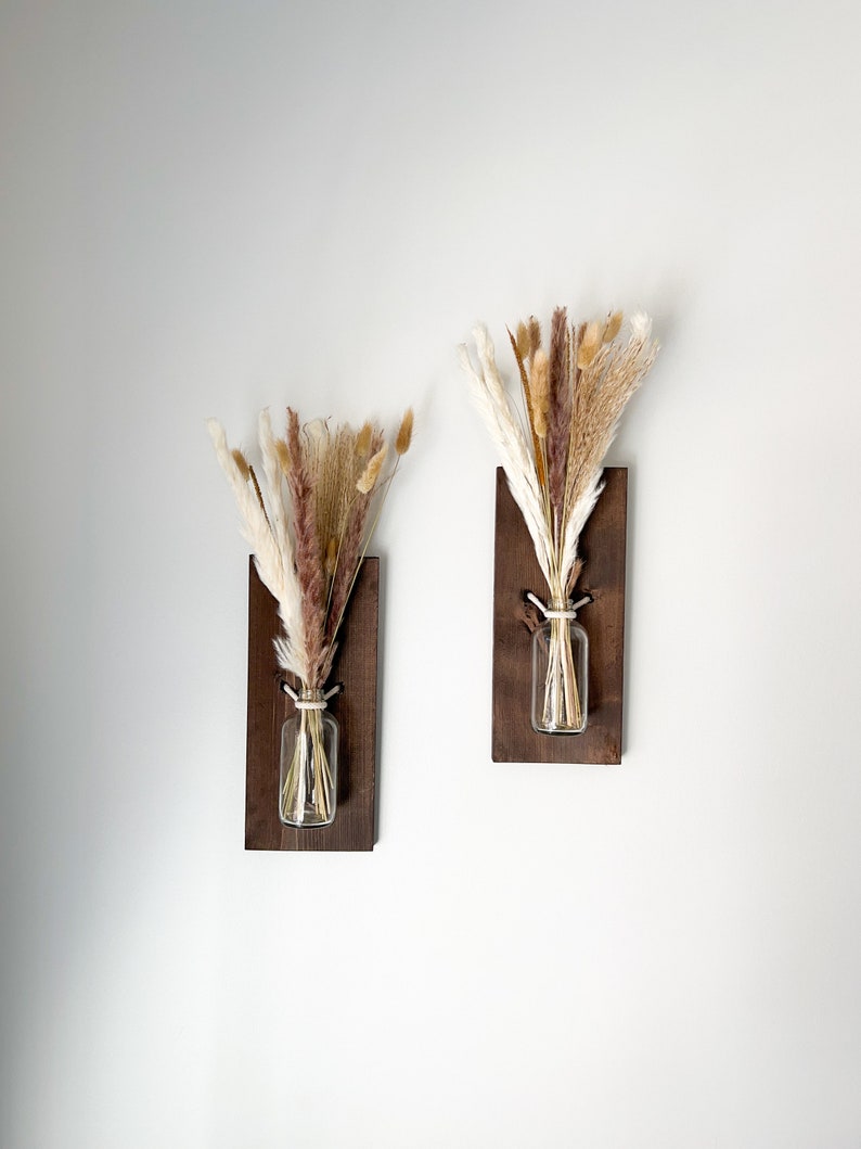 May include: Two wooden wall mounted vases with dried pampas grass in clear glass bottles. The vases are stained a dark brown color.