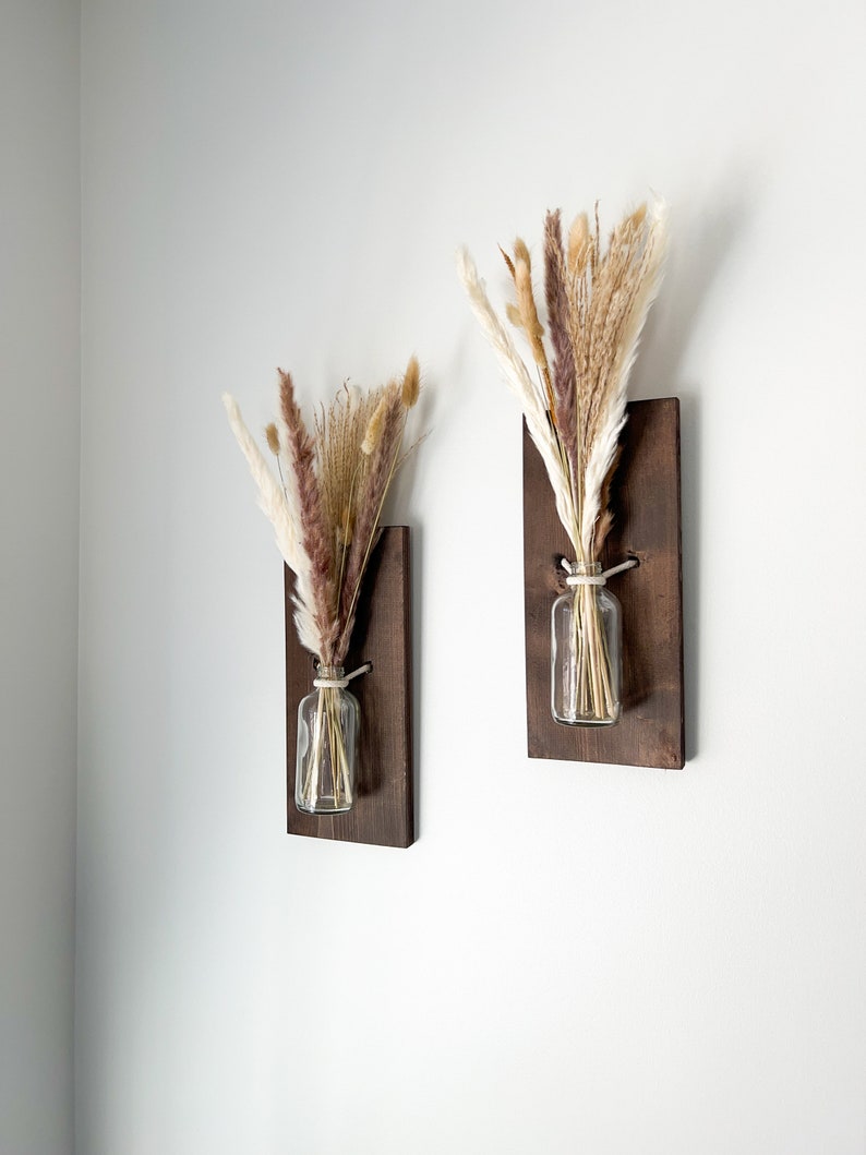 May include: Two wooden wall mounted vases with dried pampas grass in clear glass bottles. The vases are stained a dark brown color.