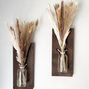 May include: Two wooden wall mounted vases with dried pampas grass in clear glass bottles. The vases are stained a dark brown color.