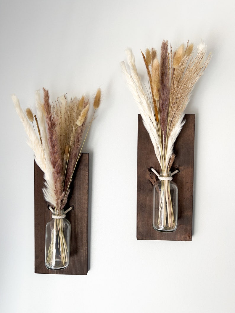 May include: Two wooden wall mounted vases with dried pampas grass in clear glass bottles. The vases are stained a dark brown color.