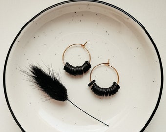 May include: A pair of gold hoop earrings with black beads. The earrings are on a white plate with a black feather.