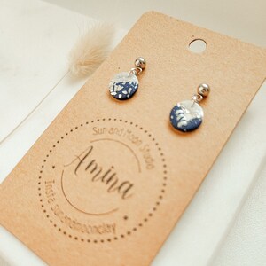 Op de afbeelding: Een paar kleine, ronde oorbellen met een wit en blauw marmerpatroon. De oorbellen zijn gemaakt van polymer clay en hebben zilveren oorhaakjes.