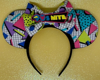 May include: A pair of black mouse ears with a white, black, pink, blue and green geometric pattern. The bow is white with black polka dots and a black and white grid pattern. The bow has a black and white patch with the text "90s Nite" in white.