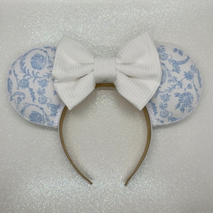 May include: White headband with a large white bow and blue and white floral fabric mouse ears.