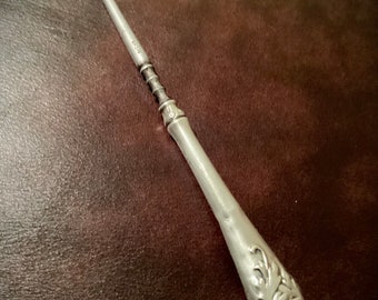 May include: A silver shoe horn with a decorative handle. The handle has a floral design and a small circle with a raised design.
