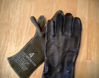 May include: A pair of gloves, one is a dark brown leather glove and the other is a green wool glove with the text "GLOVE FISERT WOOL M1949 09203 05150-71-C-1197 845 52 6516 72%VC0.28% NYLON BKZLK CLS" printed on the cuff.