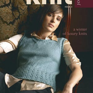 May include: A magazine cover featuring a woman wearing a teal knitted vest, sitting in a chair. The magazine is titled "knit" and the subtitle is "a winter of luxury knits". The magazine cover also states "39 hand knitting patterns" and "JO SHARP ISSUE 3".
