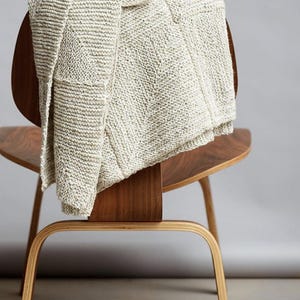 May include: A cream-colored knitted throw blanket draped over a wooden chair with a curved back and legs.