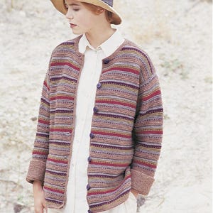 May include: A multi-colored striped cardigan with a button-up front. The cardigan features shades of red, purple, and brown. The person is wearing a white collared shirt and a straw hat with a dark blue band.