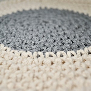 Puede incluir: Una alfombra redonda de crochet con un centro gris y un borde exterior crema.