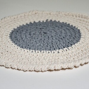 Puede incluir: Un posavasos redondo de ganchillo con un centro gris y un anillo exterior blanco.