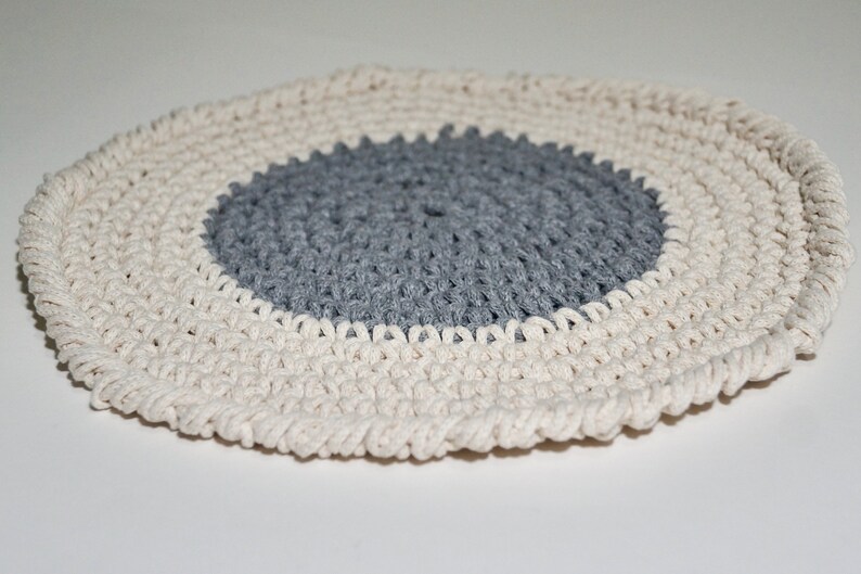 Puede incluir: Un posavasos redondo de ganchillo con un centro gris y un anillo exterior blanco.