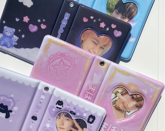May include: Several small photo albums in various colors are displayed. The albums have heart-shaped cutouts revealing photos. Designs include clouds, stars, bears, and Japanese text. The albums are in shades of blue, black, pink, and purple.