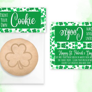 Può includere: Un sacchetto di plastica trasparente con un biscotto all'interno. Il biscotto è decorato con un trifoglio. Il sacchetto ha un'etichetta che dice "Dipingi il tuo biscotto" e "Buon San Patrizio!" con un motivo a trifoglio.