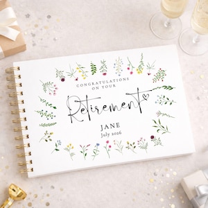 May include: A white spiral-bound guest book featuring a watercolour floral border. The text reads: CONGRATULATIONS ON YOUR RETIREMENT, JANE, July 2026. The cover is decorated with various small, colourful wildflowers and greenery arranged in a rectangular frame.