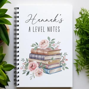 May include: A white spiral-bound notebook featuring the text Hannah's A LEVEL NOTES in black ink. The cover displays a watercolour illustration of a stack of five books in shades of brown, blue, and purple, accented with pink roses and green leaves.