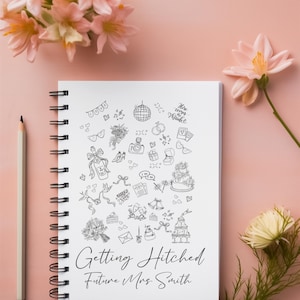May include: A white spiral-bound notebook with black line art illustrations of wedding-related icons, including a cake, rings, and flowers. The text "Getting Hitched Future Mrs. Smith" is written below the illustrations. A pencil and pink flowers are also in the image.